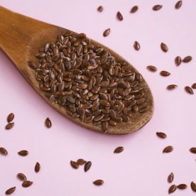 Flax seed in spoon on pink background. Healthy food.